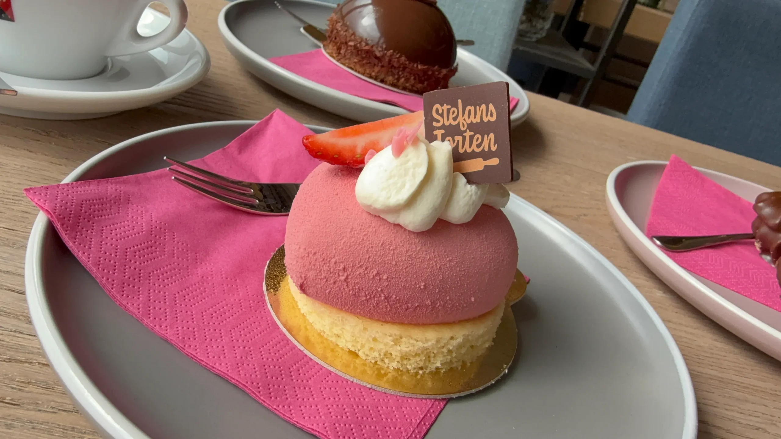 Kaffee und feine Törtchen von Stefans Torten auf Tellern mit pinker Serviette.