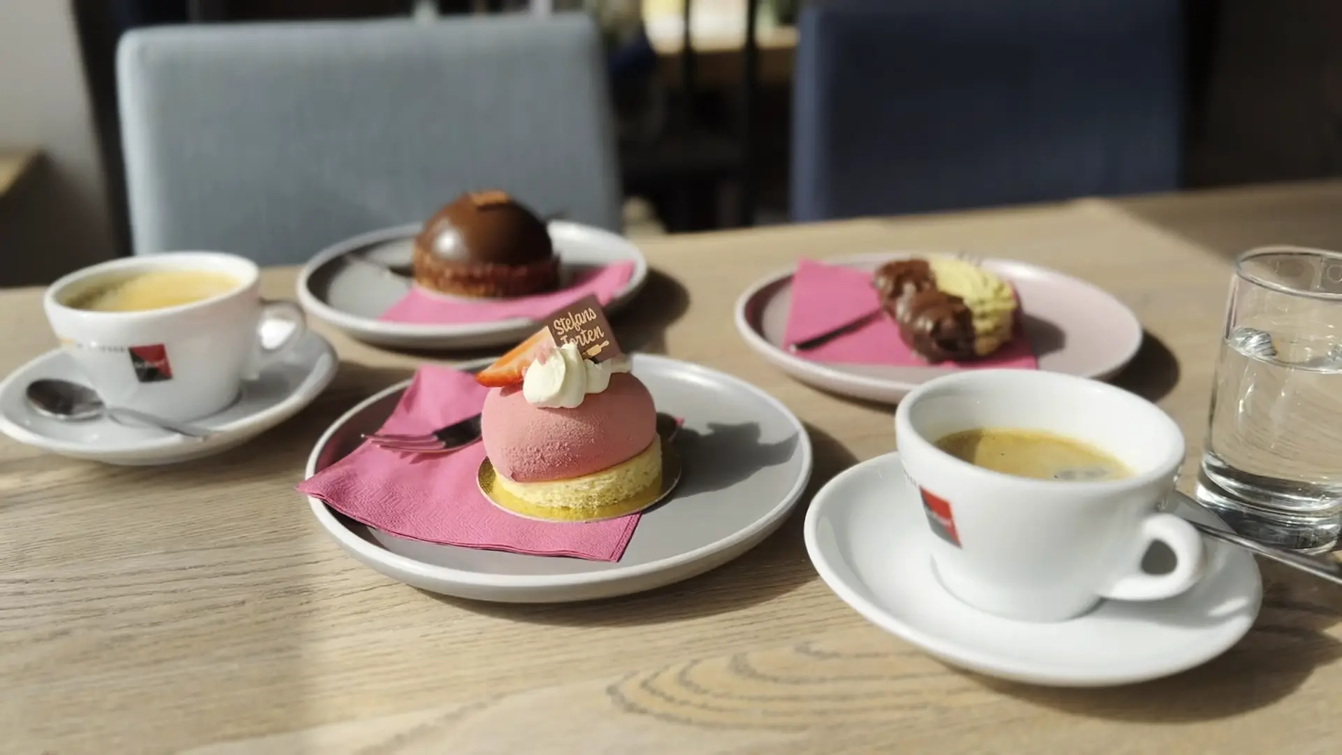 Kaffee und feine Törtchen von Stefans Torten auf Tellern mit pinker Serviette.