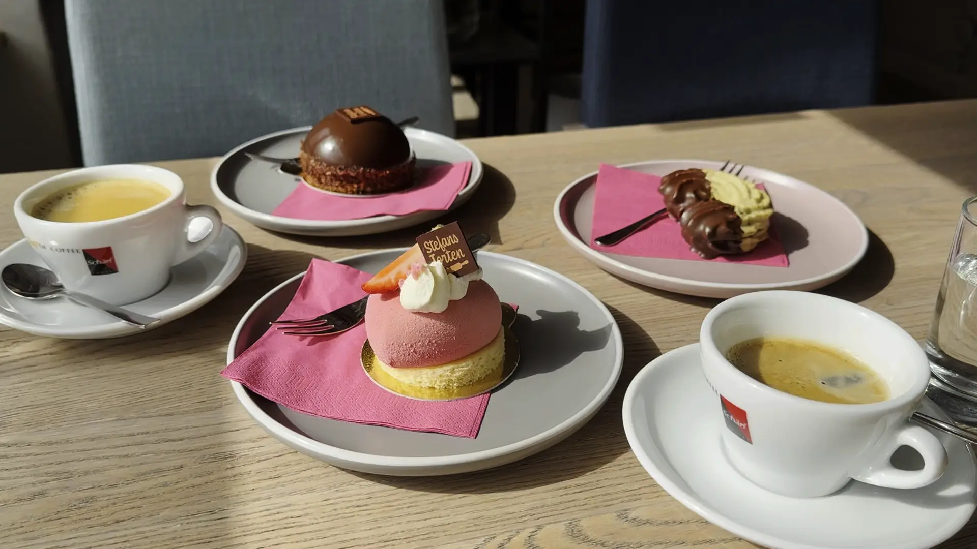 Kaffee und feine Törtchen von Stefans Torten auf Tellern mit pinker Serviette.