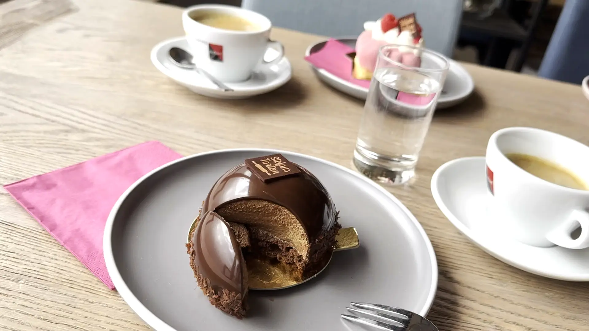 Kaffee und feine Törtchen von Stefans Torten auf Tellern mit pinker Serviette.