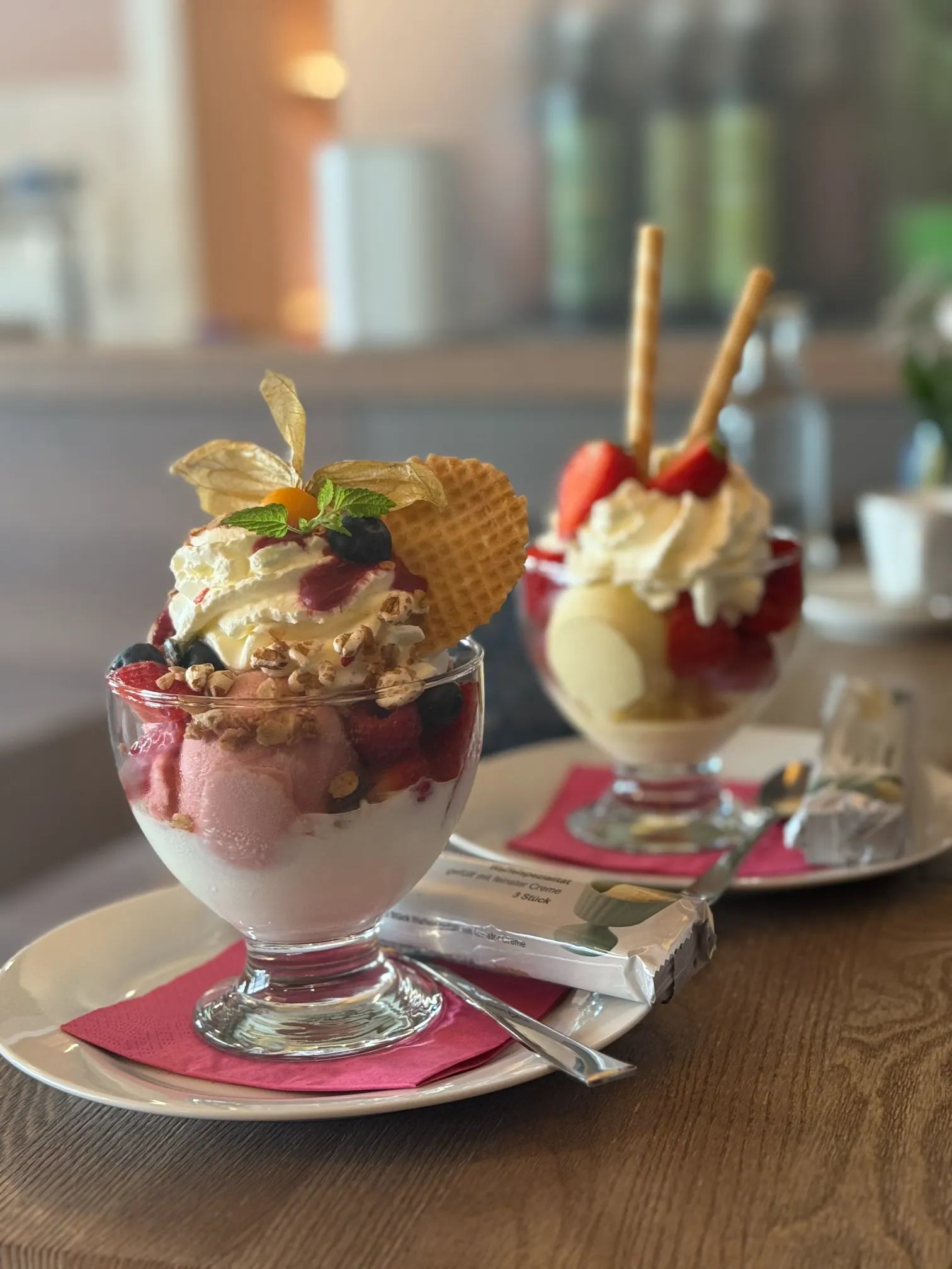 Zwei Eiskreationen im Glas – Himbeer-Joghurt und Erdbeereis liebevoll dekoriert mit Beeren und Sahne